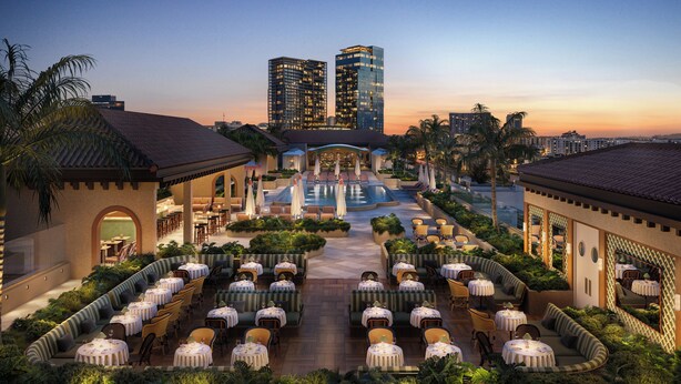 Un hotel con mesas al aire libre, piscina y edificios altos al fondo.