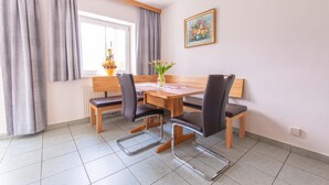 Un comedor con una mesa de madera, cuatro sillas, un banco, una ventana con cortinas y un cuadro en la pared.