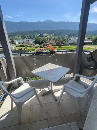 A balcony with two white plastic chairs and a small table, overlooking a scenic view of a lake and mountains.