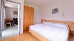 Una habitación de hotel con una cama, un armario de madera, un escritorio con una silla y un cuadro en la pared.