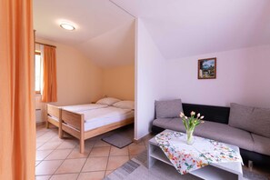 A room with a bed, a sofa, a small table with a floral tablecloth, and a painting on the wall.