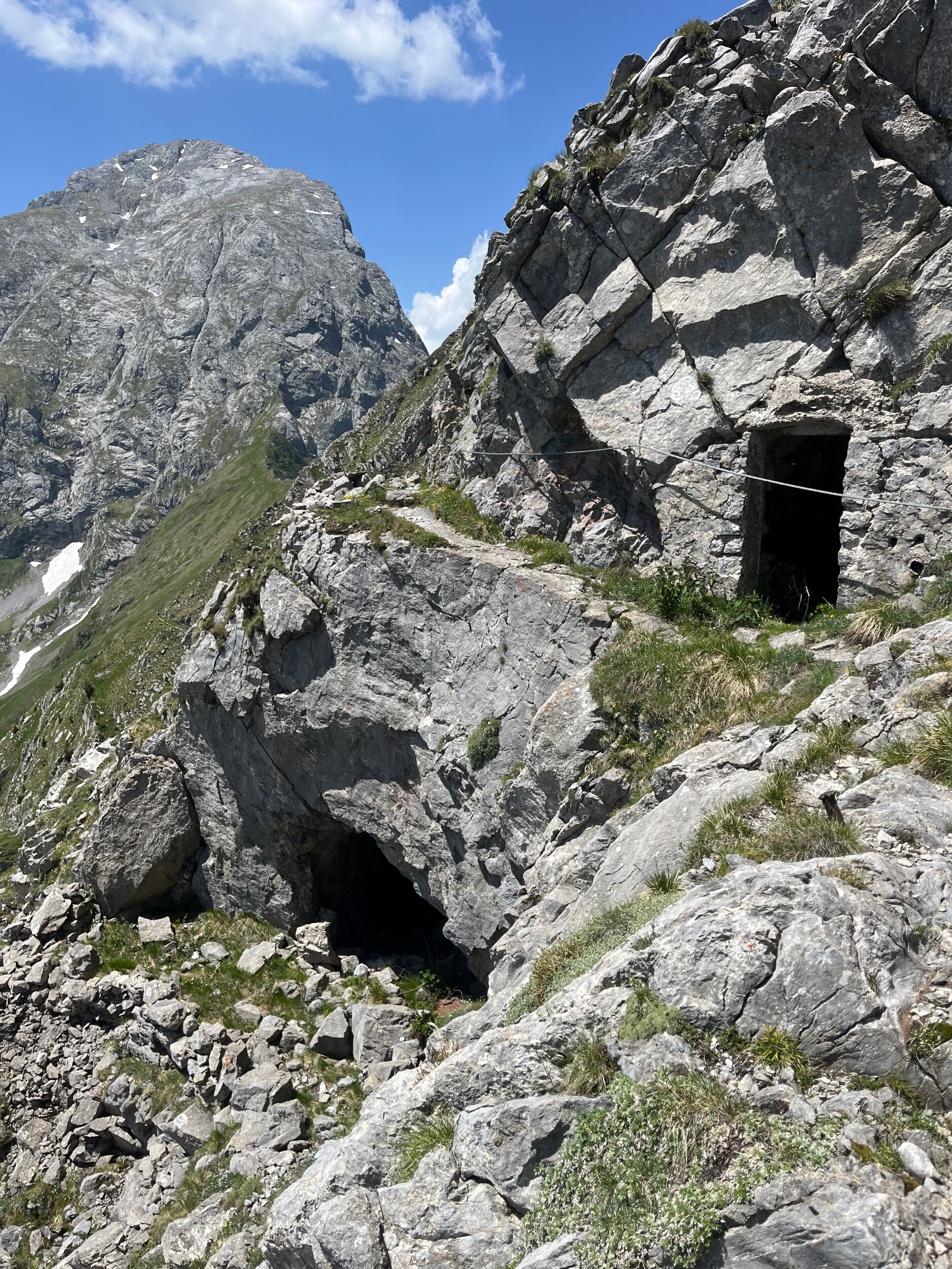 Un paisaje montañoso y agreste con terreno rocoso, un sendero estrecho y una pequeña estructura parecida a una cueva.