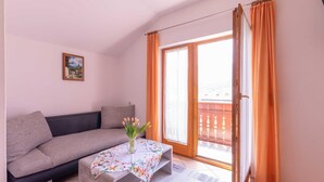 Quarto com sofá, mesa com toalha florida, um vaso de flores, um quadro na parede e uma porta de vidro deslizante com cortinas.