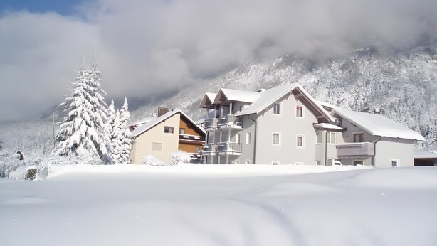 Un paisaje montañoso nevado con un edificio que tiene varios balcones y una pista de esquí al frente.
