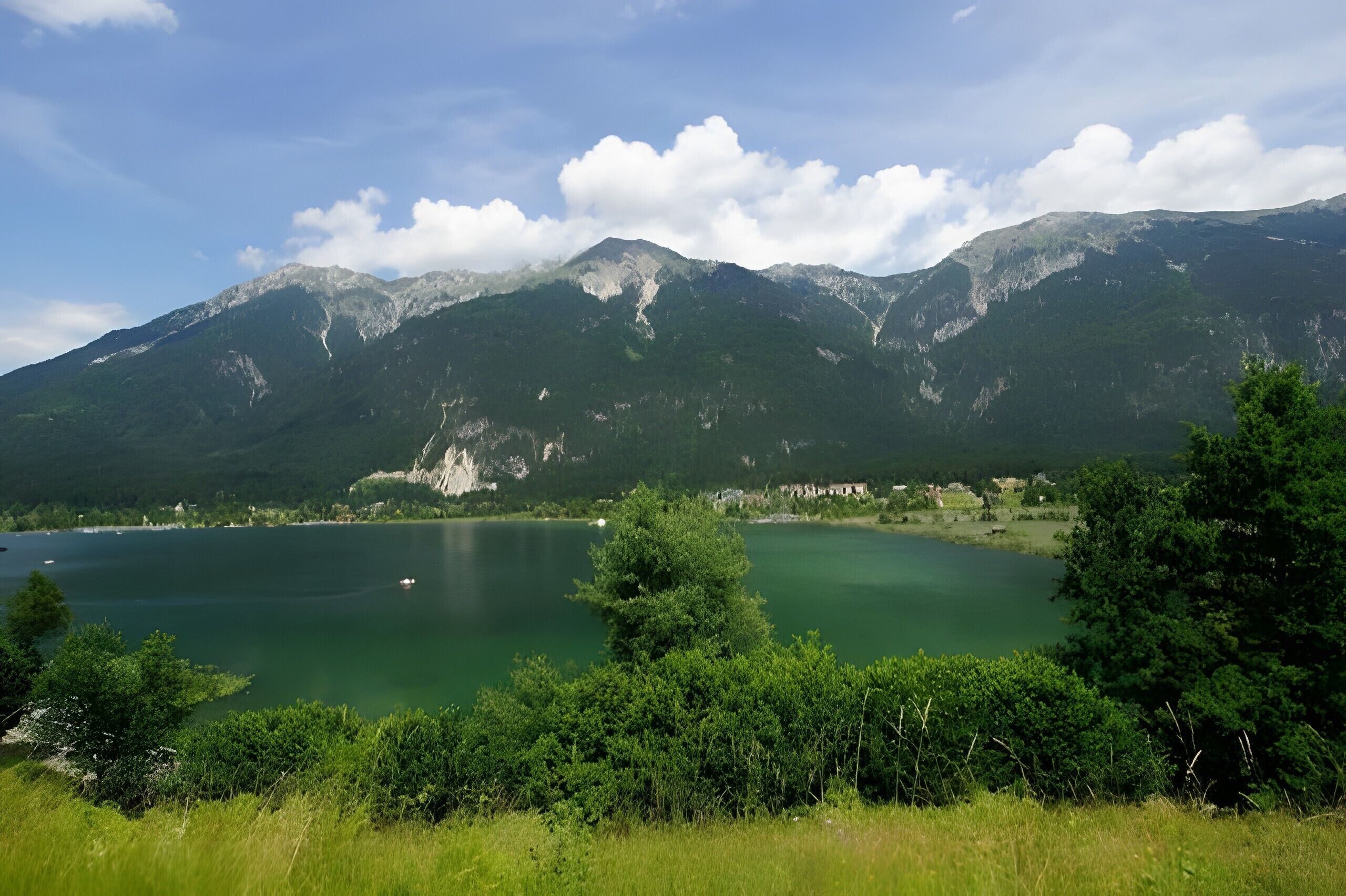A lake surrounded by mountains, with a clear sky and some clouds.