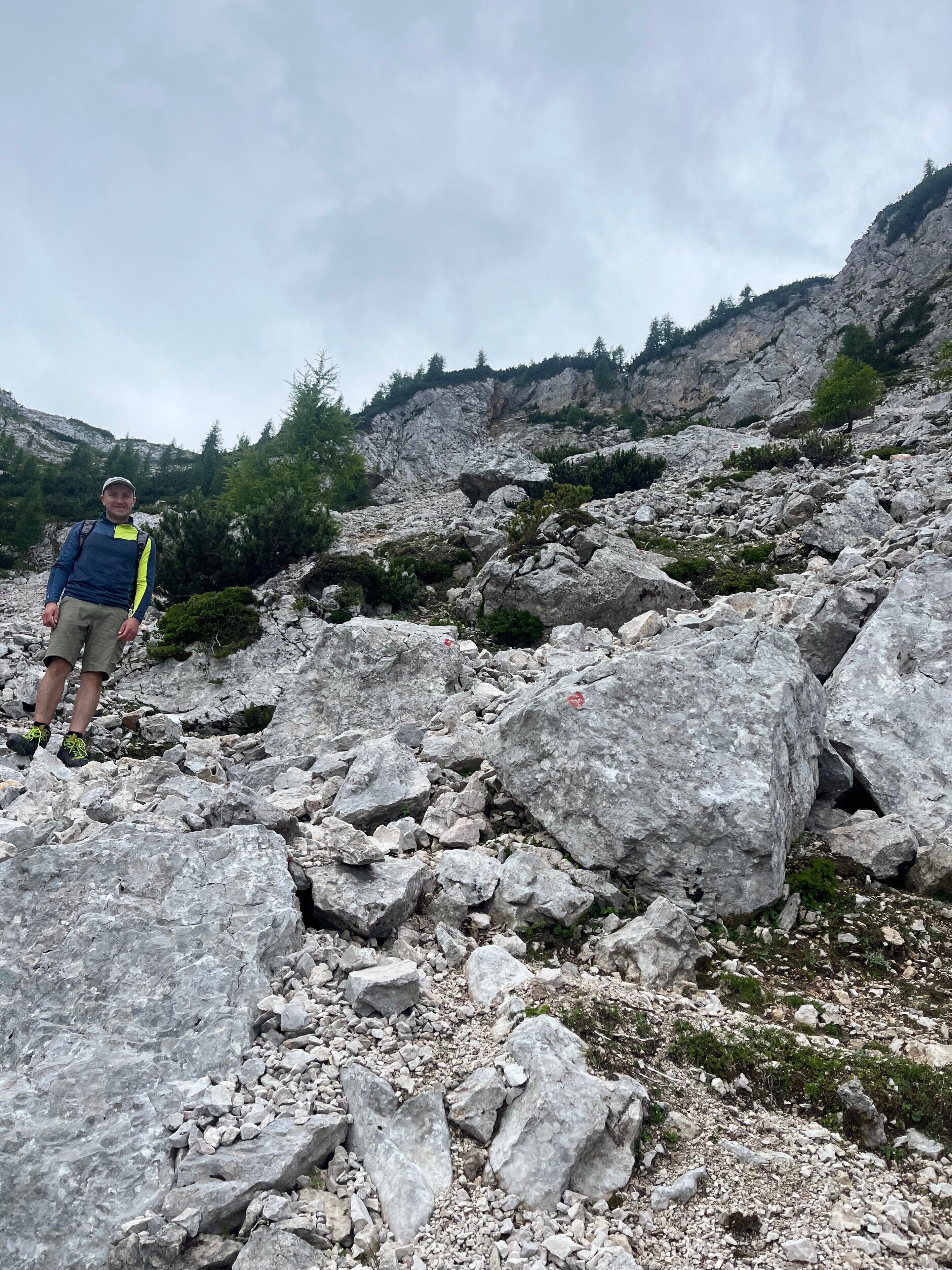 Una persona de pie sobre terreno rocoso, con grandes rocas y vegetación escasa.