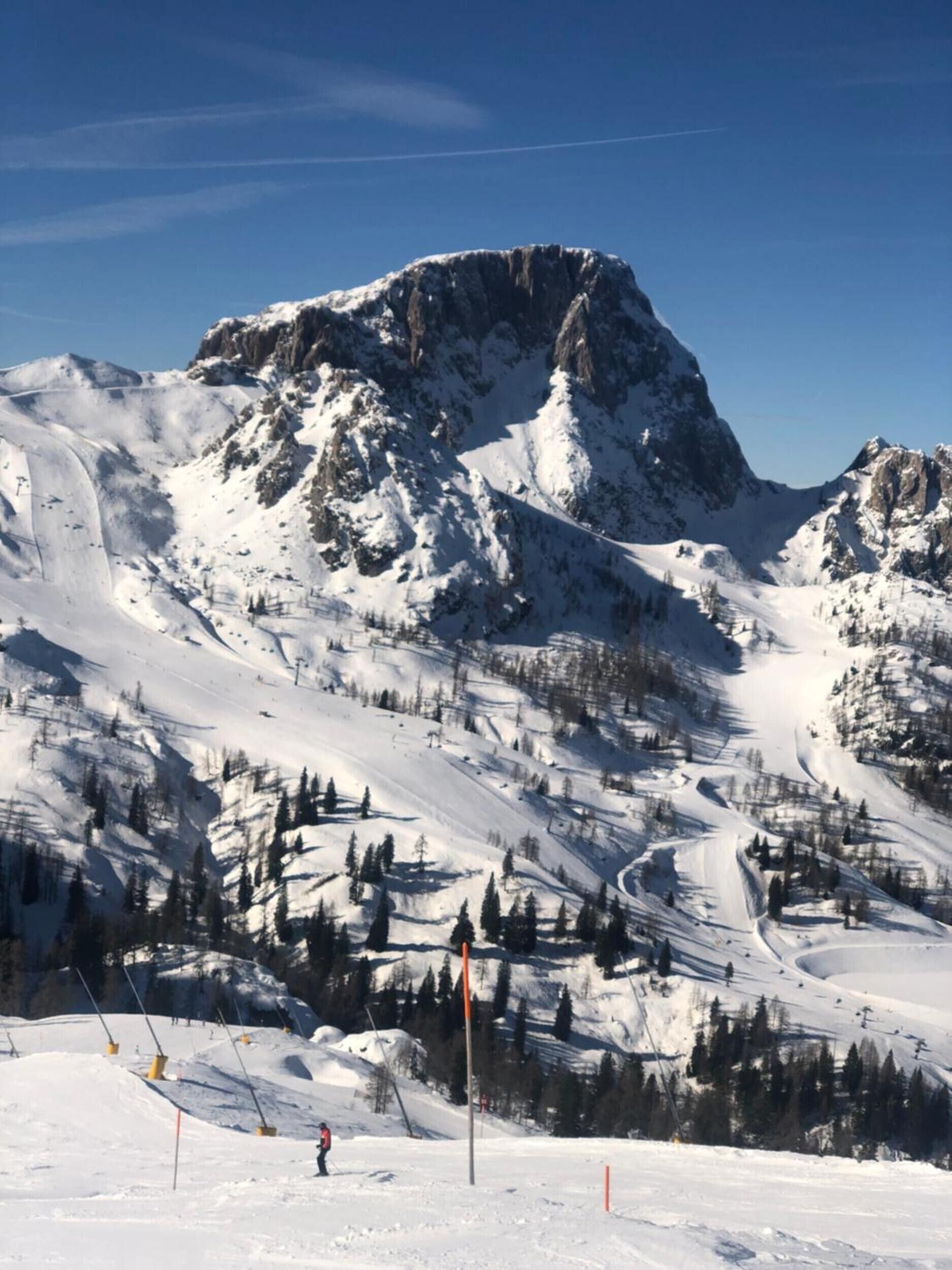 Ein mit Schnee bedeckter Berg mit Skipisten und einem klaren Himmel.
