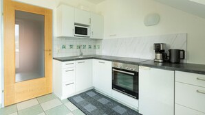 A compact kitchen with white cabinets, a microwave, an oven, a coffee maker, and a tiled backsplash.