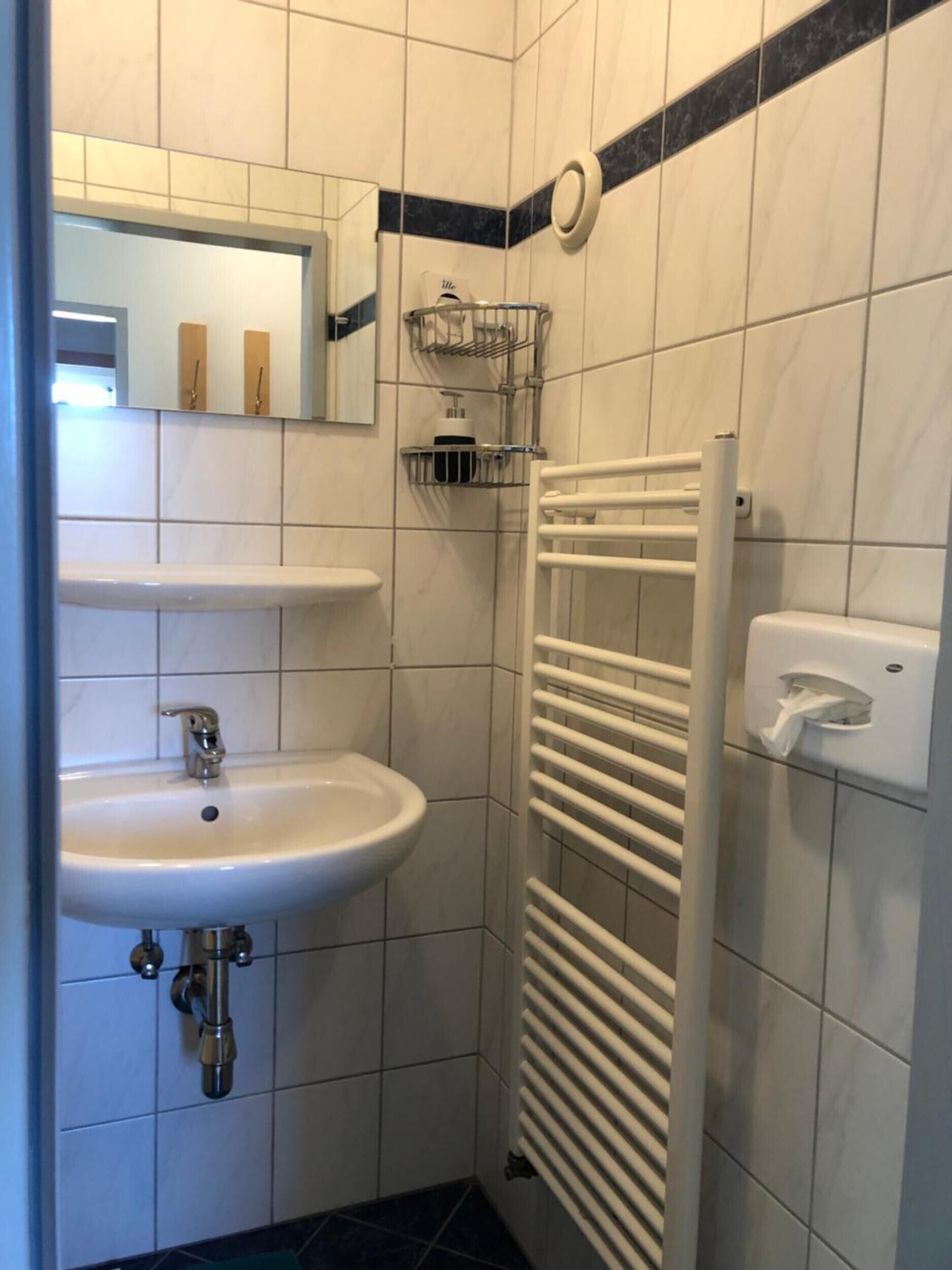 Casa de banho com lavatório branco, espelho, porta-toalhas e secador de mãos.