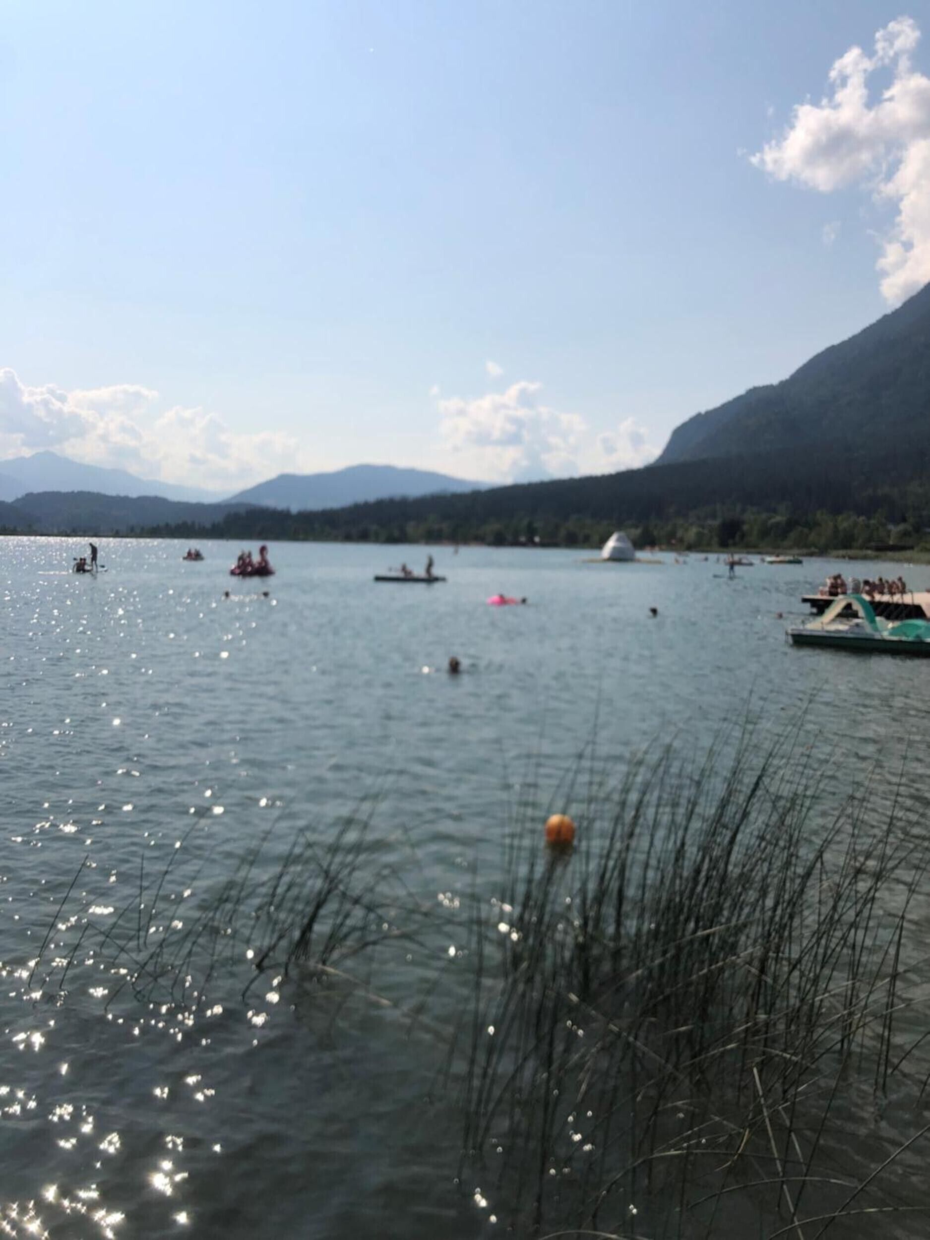 Un lago con barcos y gente, rodeado de montañas.