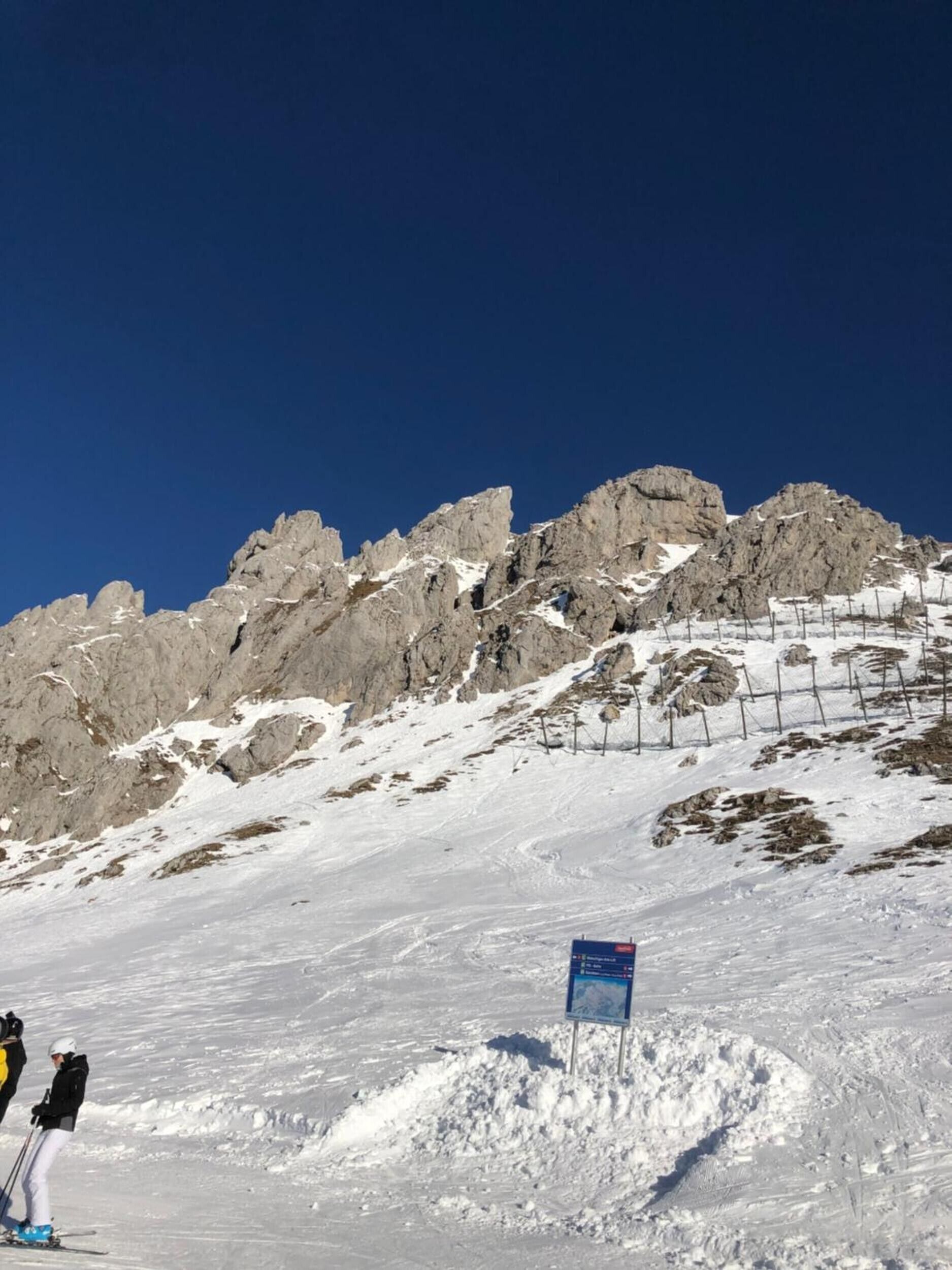 Pendiente nevada de montaña con afloramientos rocosos y cielo azul despejado.
