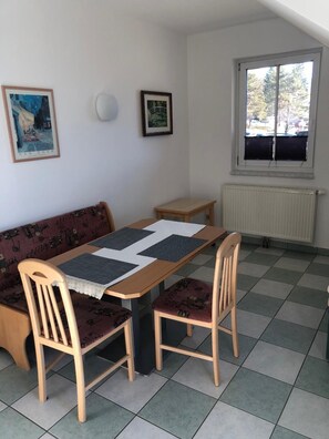 Een eetgedeelte met een tafel, stoelen, een bank en een raam met zonwering.