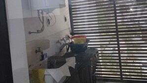 Une cuisine équipée d’un évier, d’un robinet et d’un plan de travail. Il y a une fenêtre avec des stores et une porte donnant sur un balcon.