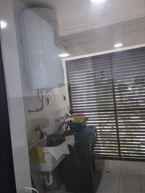 Eine Küche mit Spüle, Armatur und Arbeitsplatte. Ein Fenster mit Jalousien und eine Tür, die auf einen Balkon führt.