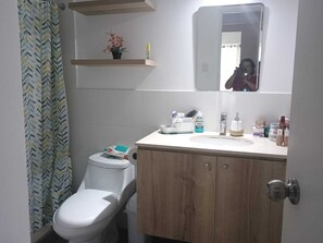 A bathroom with a toilet, a sink with toiletries, a mirror, and a shower curtain. - Charming 3-bedroom apartment in El Polo-near U.S. Embassy-perfect for groups (Lima)