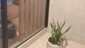 Un balcon doté d’une balustrade en verre, d’un pot de fleurs et offrant une vue sur un immeuble dont les fenêtres sont illuminées.
