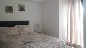 Une chambre à coucher avec un lit, une table de chevet, une lampe et une fenêtre avec des rideaux.