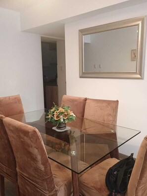 A dining area with a glass table surrounded by velvet chairs, a vase with flowers, and a framed mirror on the wall. - Charming 3-bedroom apartment in El Polo-near U.S. Embassy-perfect for groups (Lima)