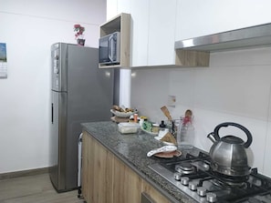 Eine Küche mit Edelstahlkühlschrank, einer Mikrowelle, einem Gasherd und einem Holzschrank über der Arbeitsfläche.