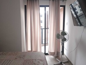 A bedroom with a bed, a standing fan, and a TV mounted on the wall. - Charming 3-bedroom apartment in El Polo-near U.S. Embassy-perfect for groups (Lima)