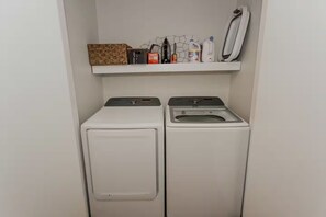 A laundry area with two washing machines, a shelf with cleaning supplies, and a drying rack.