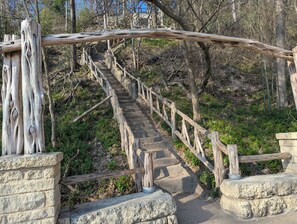 Una escalera de madera con diseño natural y rústico, rodeada de barandas de piedra y un área boscosa.
