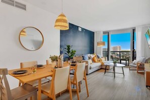 A modern living room with a dining area, large windows, and a city view. - Resort-Style Condo | Balcony | Pool & Family Vibe (Hallandale Beach)