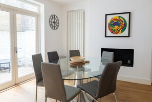 A modern dining room with a glass table, four chairs, a bowl, a clock, and a colorful artwork. - Two tube stations on your doorstep — period charm, sleeps 6 (Greater London)