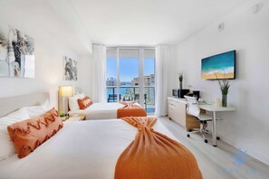 A hotel room with two beds, a desk, a TV, and a balcony with a city view. - Amazing Apartment, Pool and Gym.-Balcony View (Hallandale Beach)