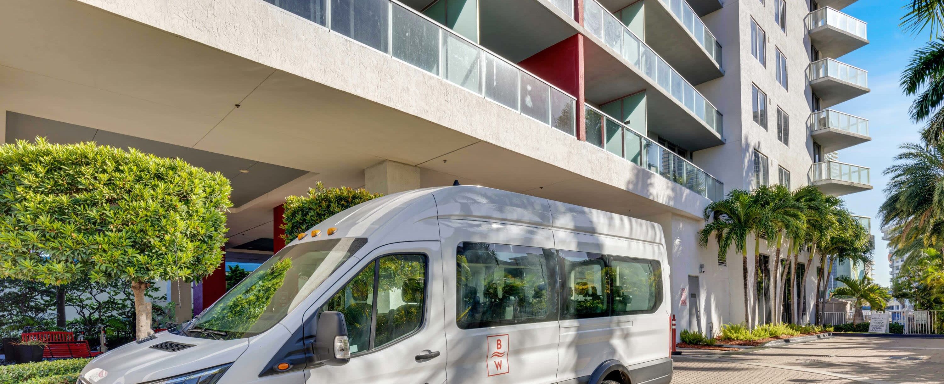 A white van parked in front of a modern building with balconies and a tree.