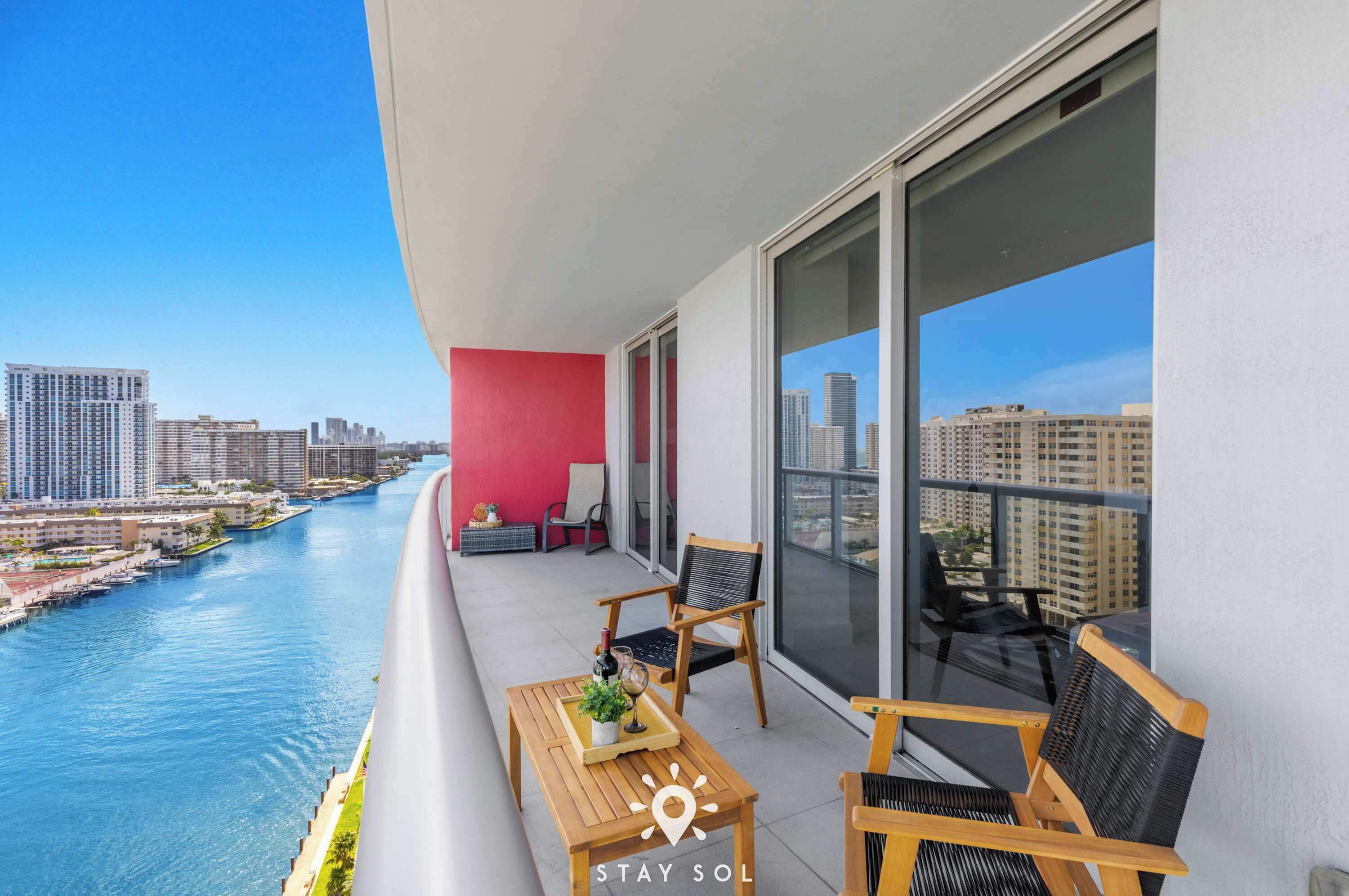 A balcony with a city view, a table with a bottle and glasses, and two chairs.