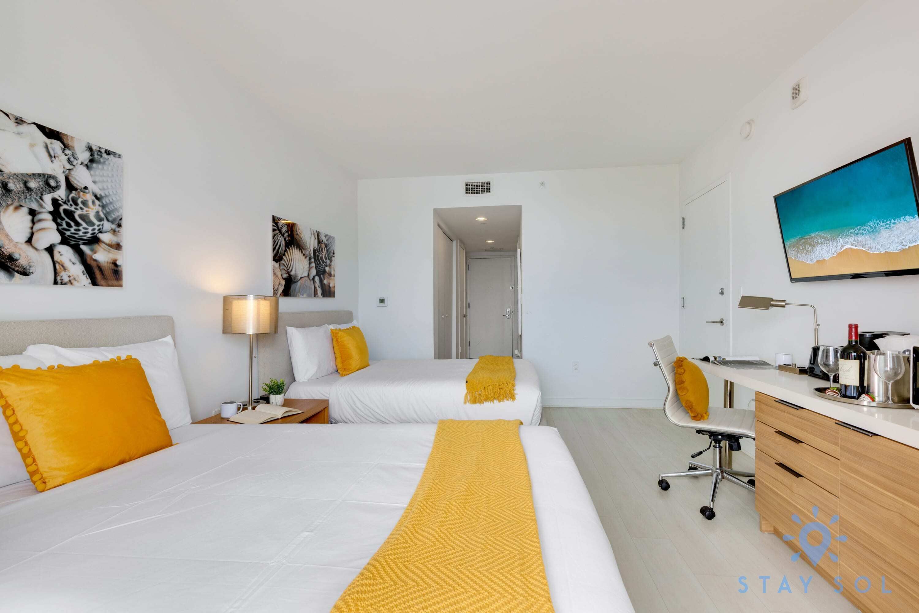 A hotel room with two beds, a desk, a chair, and artwork on the walls.