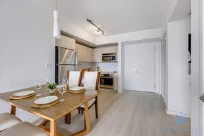 A modern kitchen with stainless steel appliances, a dining area with a wooden table and chairs, and a white door in the background. - Resort-Style 2BR | Views | Pool & Gym (Hallandale Beach)