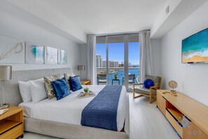 Ein modernes Hotelzimmer mit einem großen Bett, einem Schreibtisch und Blick auf Stadt und Wasser.