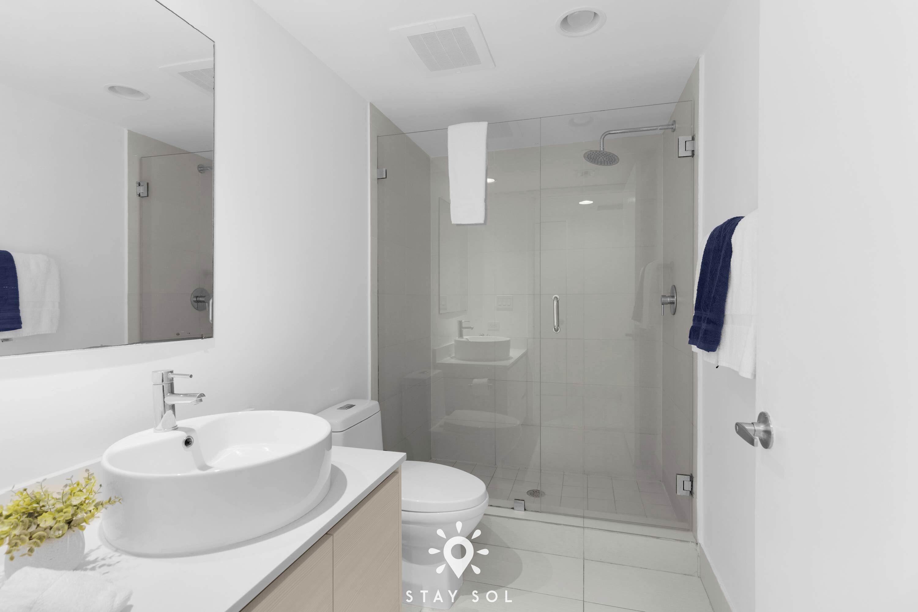 A modern bathroom with a large white sink, a toilet, and a glass-enclosed shower.