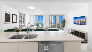 A modern kitchen with a built-in dishwasher, a dining area with green chairs, and a large window with a city view.