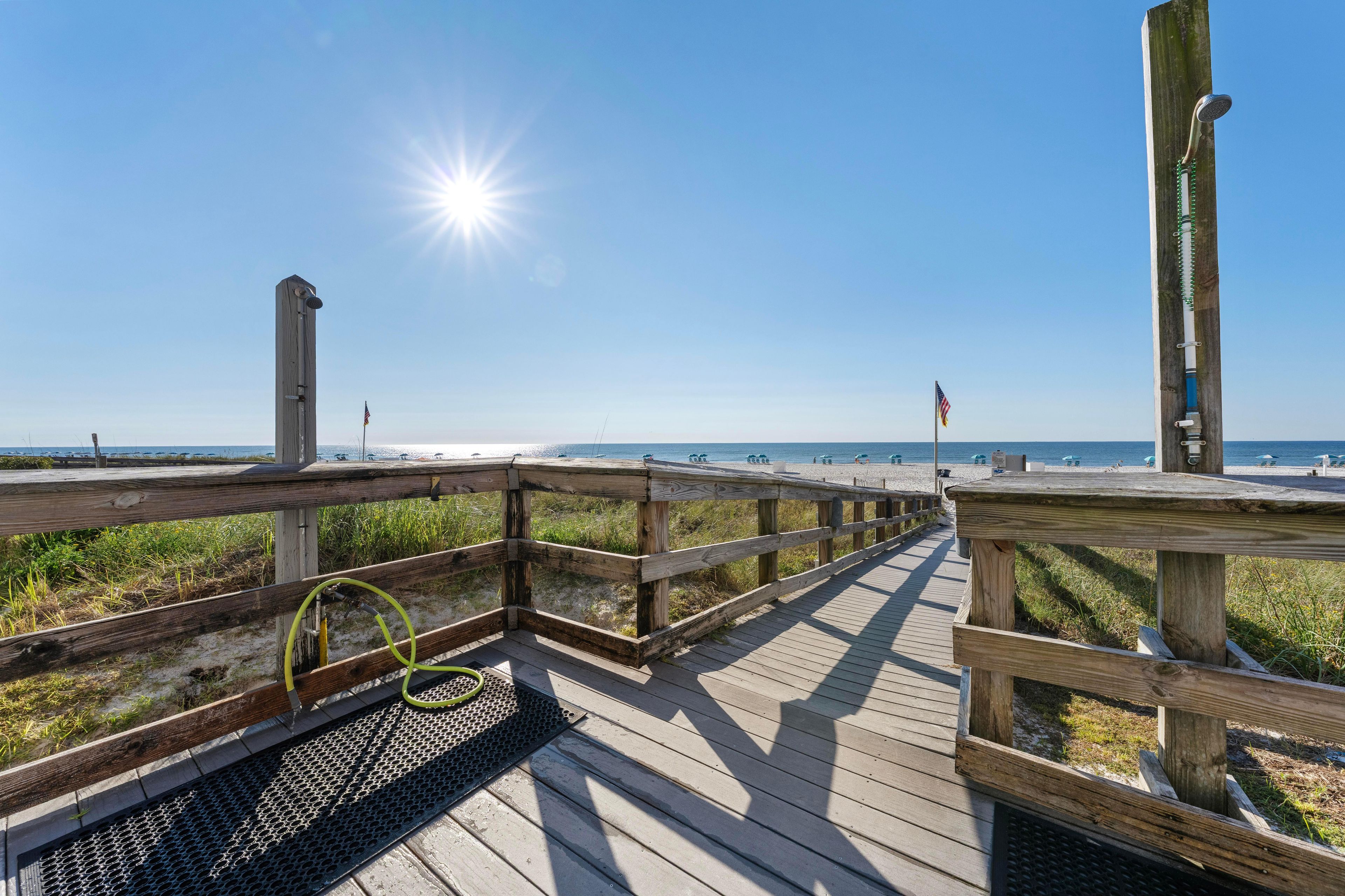 A wooden boardwalk leading to a beach with a clear sky and sun shining.