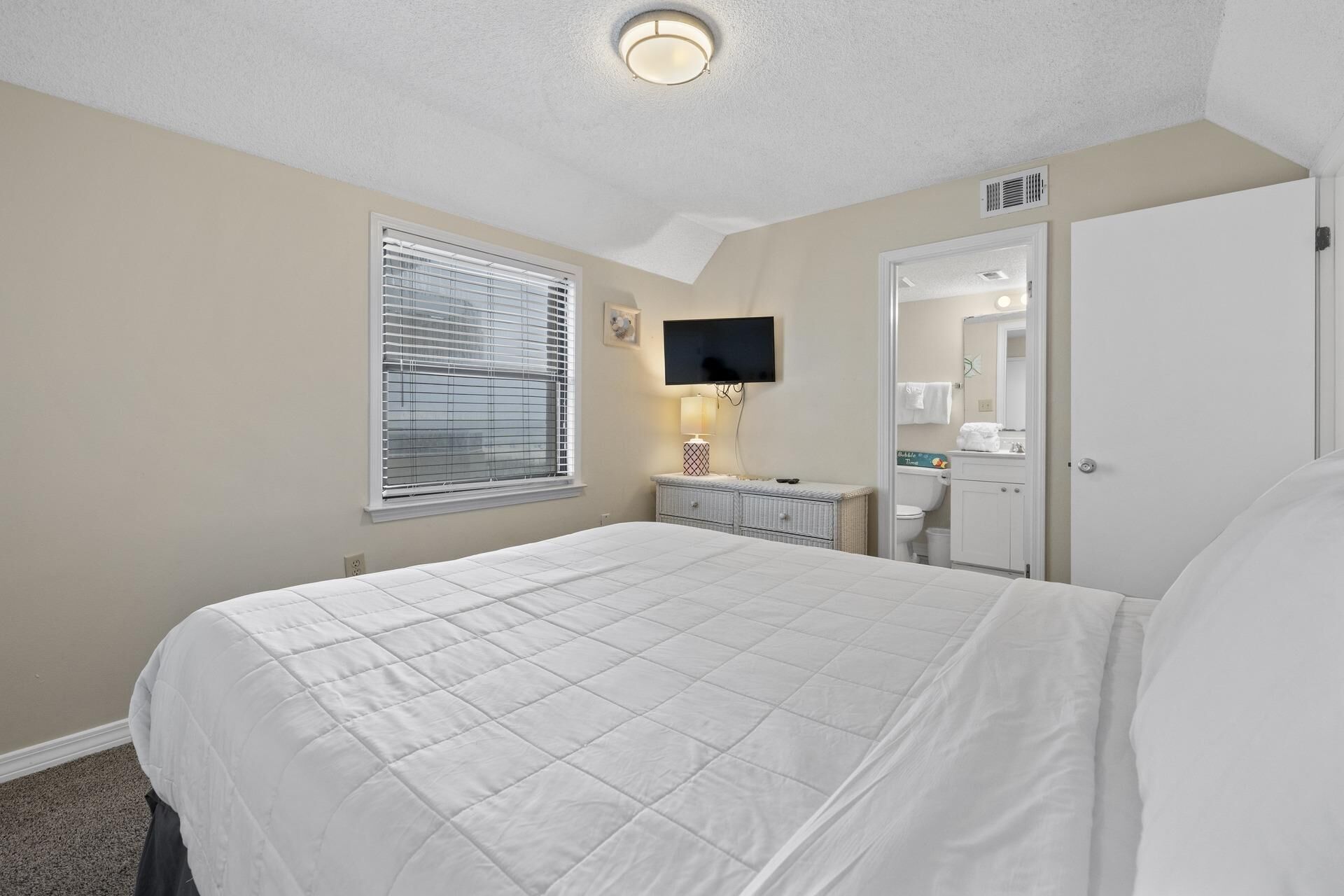 Une chambre à coucher avec un lit, une télévision, une table de chevet et une salle de bain visible à travers une porte ouverte.