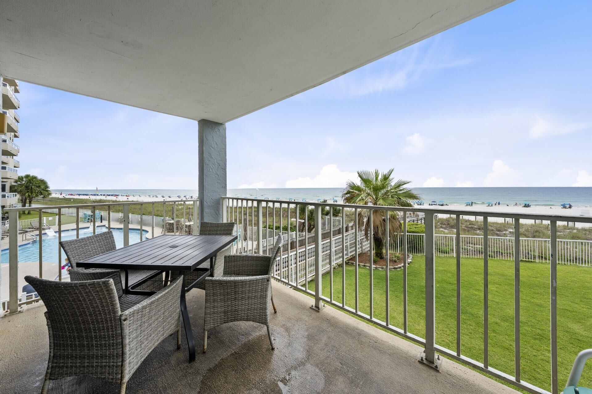 Ein Balkon mit Blick auf den Strand, ein Pool und eine Essecke mit Rattanmöbeln.
