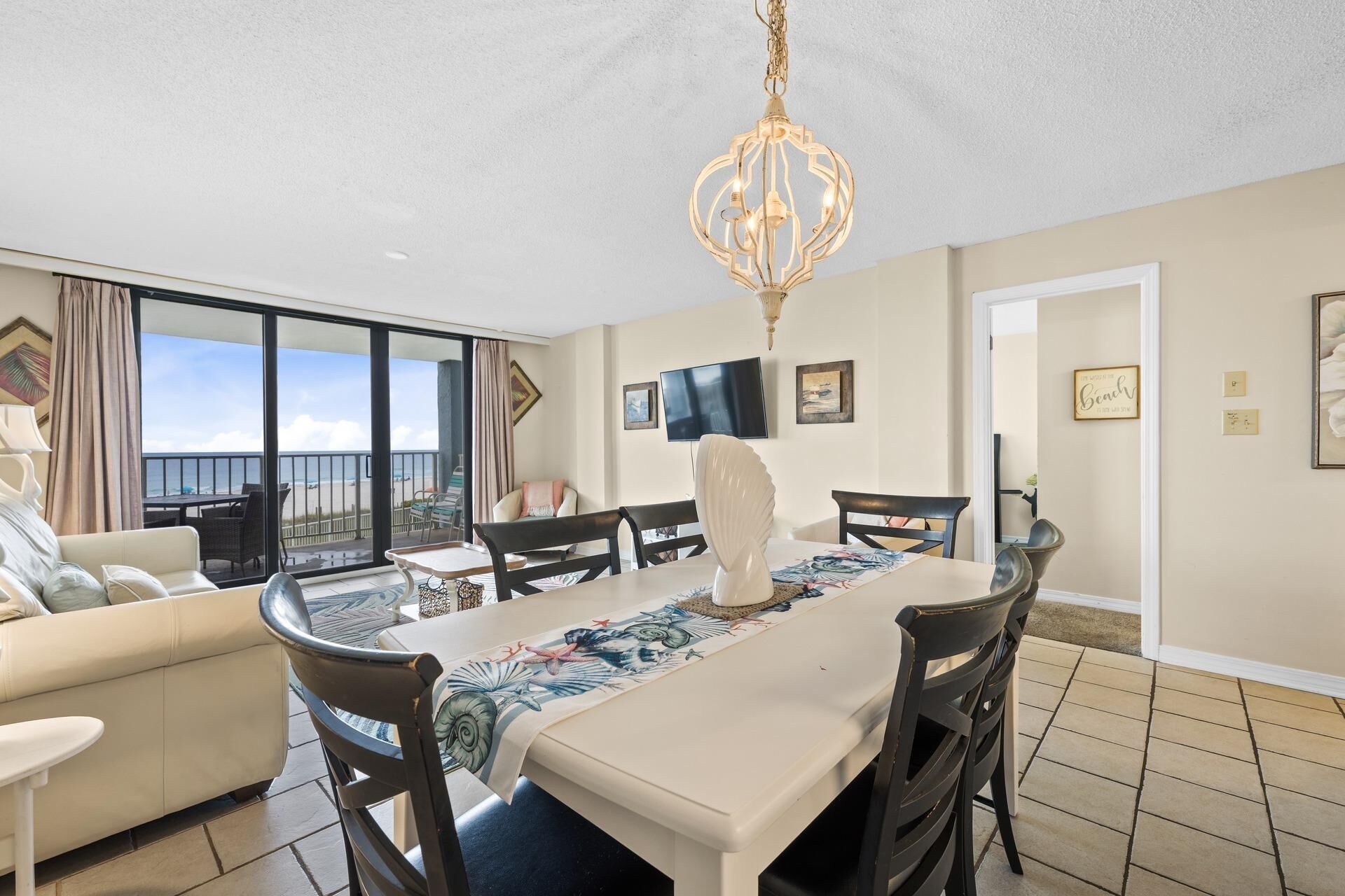 A spacious room with a balcony, a dining table, and a TV mounted on the wall.