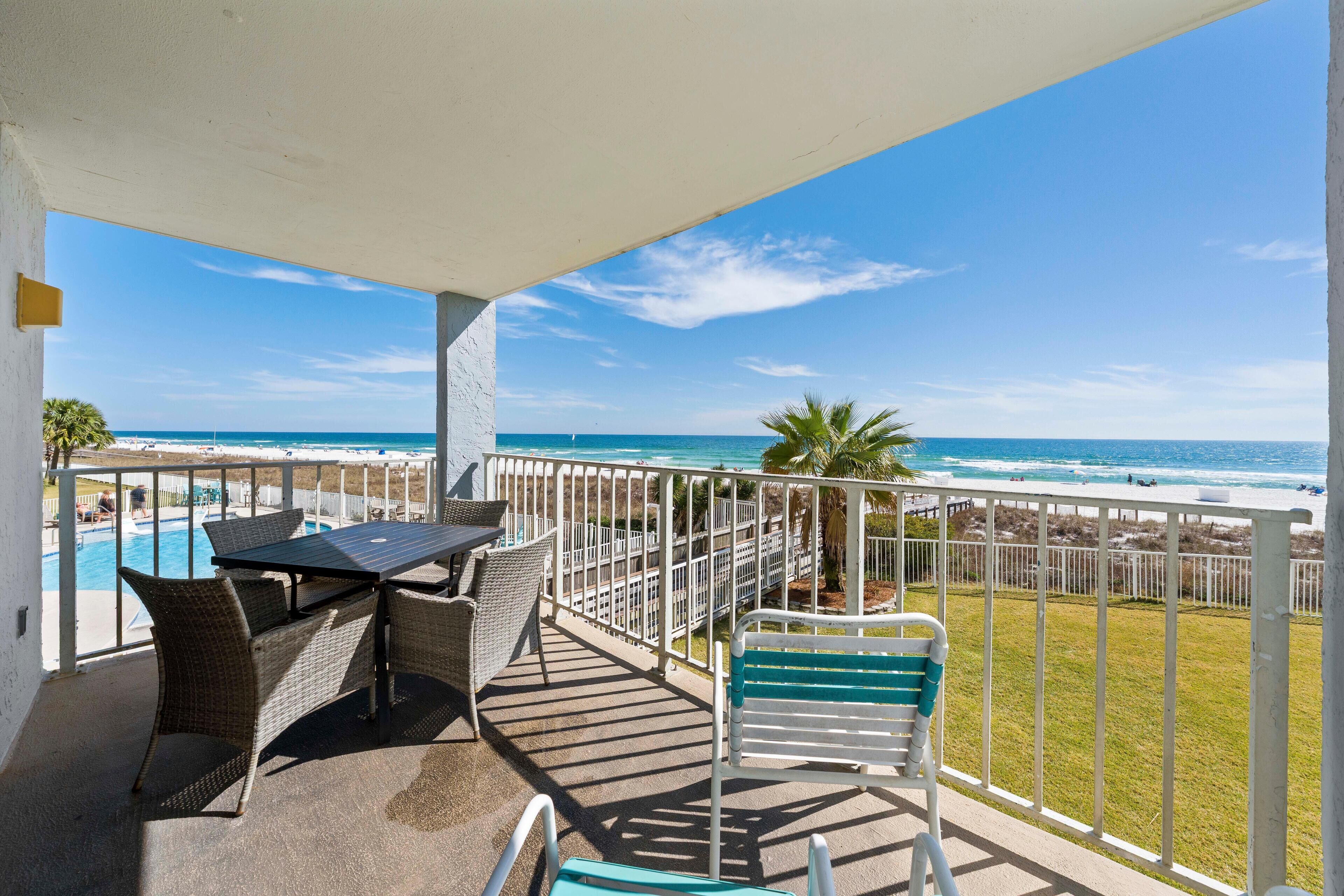 A balcony with a view of the ocean, a pool, and outdoor furniture.