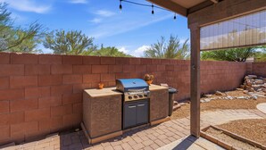 An outdoor barbecue area with a grill, oven, and string lights. - Your Cozy Desert Retreat – Pool • Fire Pit • Convenient Location (Green Valley)
