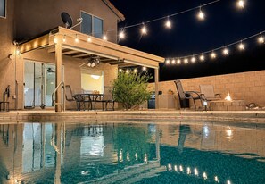 A poolside area with a covered patio, outdoor furniture, and string lights.