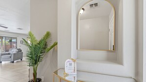 A modern interior with a potted plant, a glass console table, and a large mirror. - Your Cozy Desert Retreat – Pool • Fire Pit • Convenient Location (Green Valley)