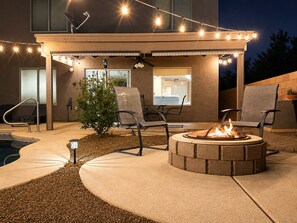 An outdoor patio with a fire pit, seating, and string lights. - Your Cozy Desert Retreat – Pool • Fire Pit • Convenient Location (Green Valley)