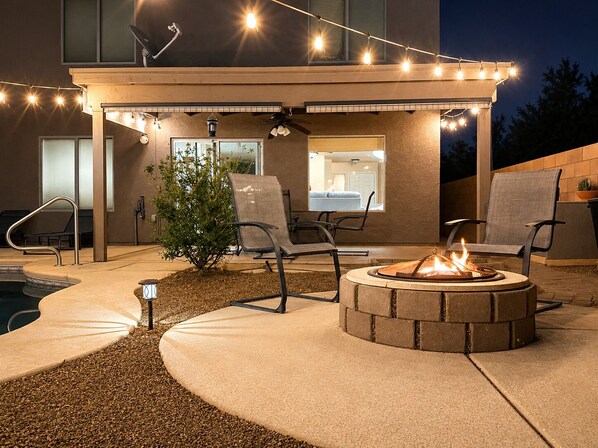 An outdoor patio with a fire pit, seating, and string lights.