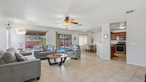 A spacious living room with a ceiling fan, a dining area, and a kitchen visible through an open doorway. - Your Cozy Desert Retreat – Pool • Fire Pit • Convenient Location (Green Valley)