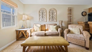 Un salon avec un canapé beige, un fauteuil assorti, une table basse en bois et deux éléments décoratifs fixés au mur.
