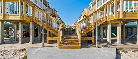 A wooden boardwalk leading to a beachfront property with multiple balconies and a clear sky.