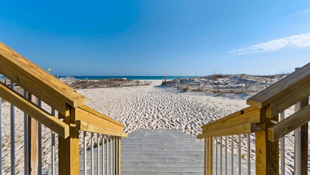 Un escalier en bois menant à une plage de sable fin, sous un ciel dégagé.